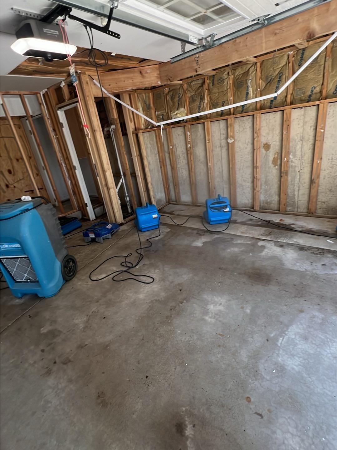 Garage stripped to the studs with air movers and a dehumidifier drying the space in a Hinsdale home