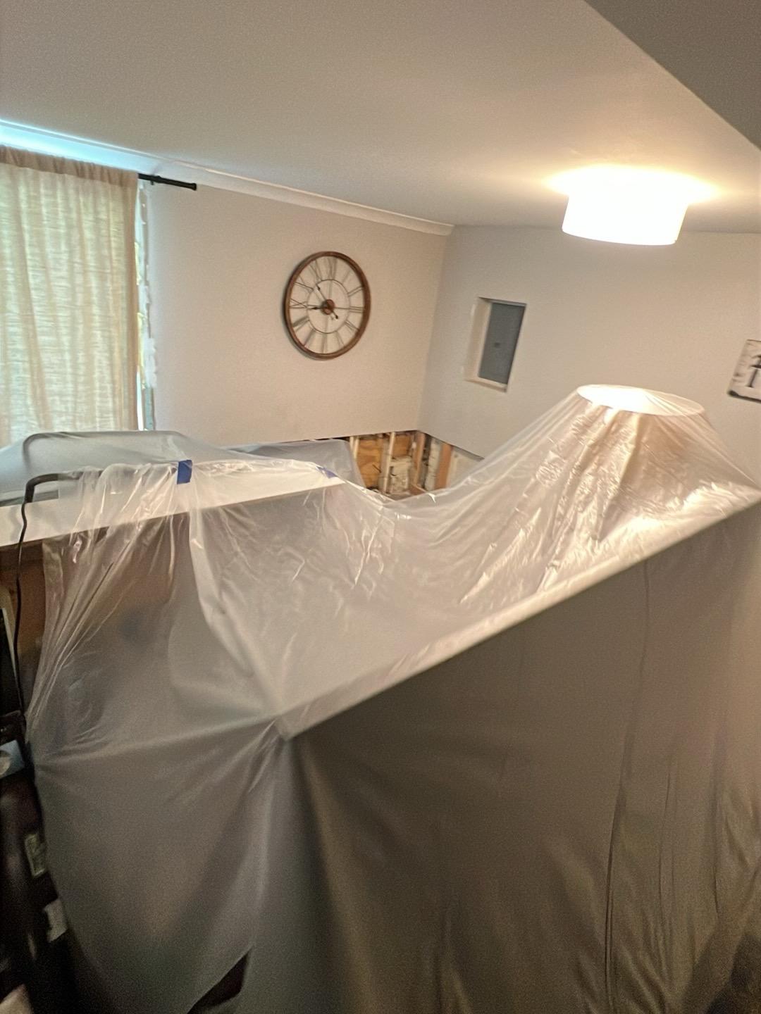 Living room furniture covered in plastic sheeting with a flood-cut wall drying in the background in a Wheaton home